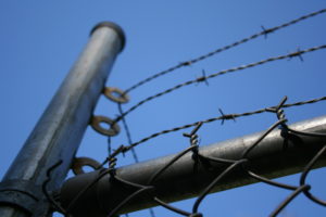 barbed-wire-converging-at-pole-against-blue-sky-full